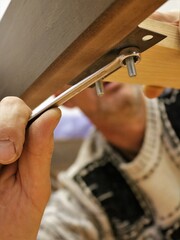 Fototapeta na wymiar tightening the fasteners with a wrench in the structure of a wooden bed bottom view, a man tightens a nut with a wrench in the process of assembling furniture, a blurry man tightens a nut