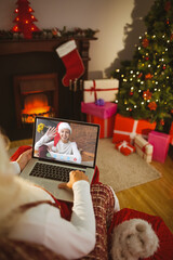 Santa claus making laptop christmas video call with waving caucasian woman in santa hat