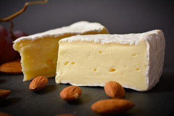 Close up of French mould cheese Brie pieces. Cheese board with soft cheese pieces. Platter served with almond nuts on black background. White soft cheese. Appetizers and starters.
