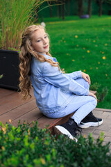 A blond-haired, blue-eyed girl sits on the threshold of the gazebo. Full-length portrait of a girl...