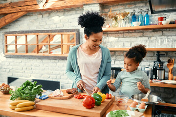 Cute black girl assists her mother in preparing food in kitchen.