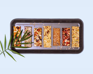 Natural granola cereal bars with nuts, seeds, oats, berries, dry fruits and palm leaf on a blue background. Energy healthy snack. Protein muesli bars. Granola superfood. Flat lay