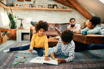 Creative black brother and sister drawing on paper while relaxing on floor at home.