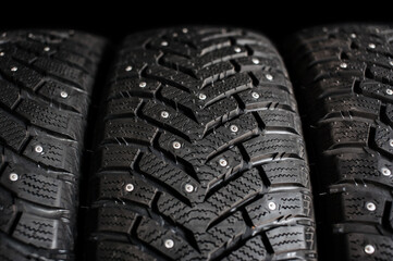 New winter car tires with spikes close-up on a black background. Tire tread. Set of winter car tires