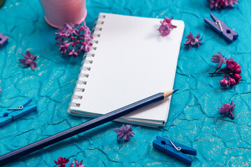 Blank notebook, pencil and lilac flowers on vintage painted blue cardboard background