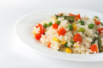 Cooked white rice mixed with colorful vegetables (onion, carrot, green peas, corn, green beans) in white plate.