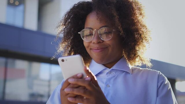 Shy pretty african american woman with afro-hair smiling reading sweet words and compliments from boyfriend, texting in online app on smartphone, flirting, virtual relations on dating web-site