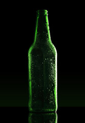 green empty bottle with drops on dark background