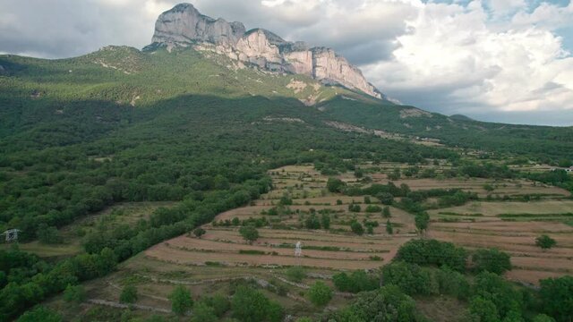 A great mountain, a rock protruding on a plateau in the Pyrenees mountains. Spectacular view of the mountain range from a drone with huge cumulus clouds in the background.