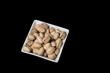Pistachios in a white plate on a black background.