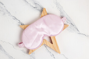 Pink sleep mask with a wooden star on a marble background. Sleep comfortably on airplane or travel,...