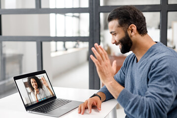 Back view of Indian man making video call to biracial female friend or coworker sitting at the desk in home office. Video communication, virtual meeting concept - Powered by Adobe