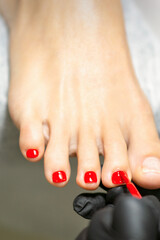 Pedicurist applying red nail polish to the female toenails in a beauty salon