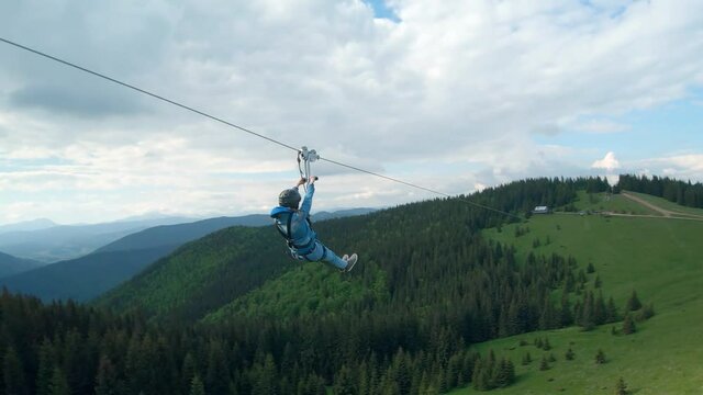 Unusual view of a woman riding a zip line among the mountains. Fast and maneuverable flight around a person. Filmed on FPV drone.