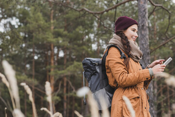 joyful woman with backpack pointing at smartphone while searching direction in forest
