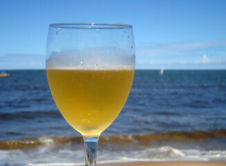 Glass of beer in front of the sea, in sunny day, blue sky, beer line matching horizon
