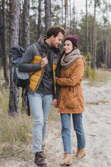 happy young couple in autumn outfit hiking in forest