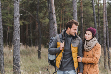 Fototapeta premium positive young couple talking while walking in autumn clothes in forest