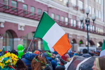 National Flag of Ireland close-up in the hands of man, crowd people, city street during celebration...