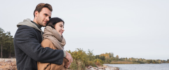 young couple in autumn outfit embracing while walking near lake, banner