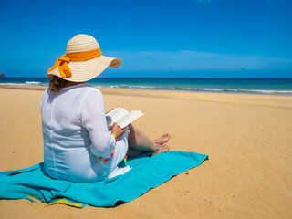 Woman sitting on beach reading book
