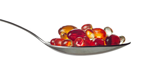 Red and orange transparent capsules with vitamins or medicine in spoon isolated