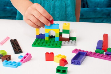 Fototapeta premium The child's hand holds a part of a colored plastic construction kit and puts it in its place.