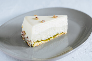 Four layer cake with pistachio, vanilla and white chocolate on grey plate with pistachios on top
