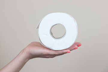 A woman's hand holds a roll of white toilet paper. Generally available household product, personal hygiene item.