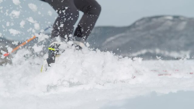 SLOW MOTION, LOW ANGLE, CLOSE UP, DOF: Female Nordic skier turns hard and sprays wet snow at camera. Woman is spraying snow with her skis during a Nordic skiing training session in Slovenian mountains