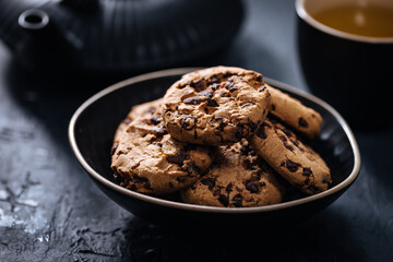 Chocolate chip cookies with tea in background in a dark moody atmosphere 