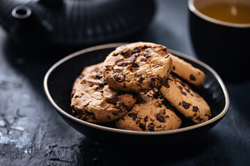 Chocolate chip cookies with tea in background in a dark moody atmosphere 