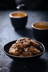 Chocolate chip cookies with tea in background in a dark moody atmosphere 