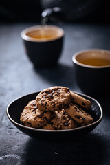 Chocolate chip cookies with tea in background in a dark moody atmosphere 