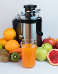 A glass of fresh fruit juice, fruits and a modern juicer extractor on the table. Healthy fruit and vegetable juices at home. Selective focus. Close-up.