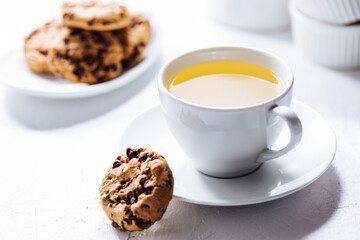 Cup of tea in white cup with chocolate chip cookies as a part of a scene, on a white background