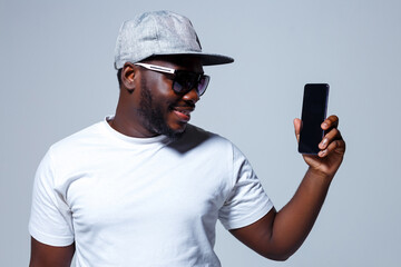 A black smiling worker is presenting his new dark phone while seriously looking at the camera.