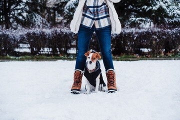 close up of happy woman wearing face mask in snowy landscape standing with cute jack russell dog during winter