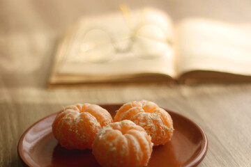 Plate of peeled tangerines, open book and reading glasses. Selective focus.
