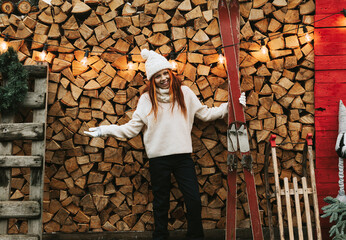 teenage girl in white knitted sweater and hat stand at porch of country house with skates, concept of winter sports and Christmas active holidays for children outdoor