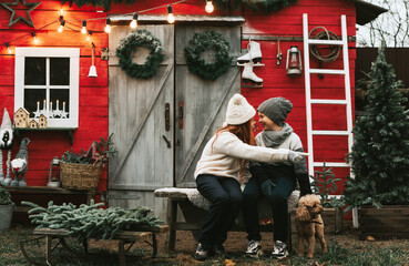 siblings teenage girl sister and cute boy brother in knitted sweater and hat having fun with first snow at porch of country house, concept of winter sports and Christmas holidays for children outdoor