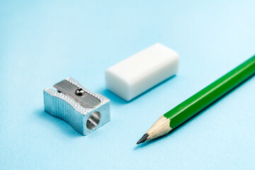 Pencil, sharpener, eraser on blue background. Green graphite pencil, education concept