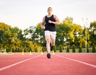 Obraz premium Young muscular fit male sprinter running on a red running track - Fitness and wellness concept with a millennial runner - Symmetrical, central composition