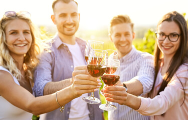 Young friends having fun outdoors - Happy people enjoying harvest time together at farmhouse winery countryside - Youth and friendship concept - Toasting red wine glass at vineyard before sunset
