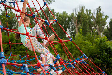 Healthy young active elementary school age girls, children climbing up high on playground...