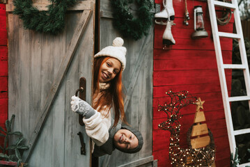 siblings teenage girl sister and cute boy brother in knitted sweater and hat having fun with first snow at porch of country house, concept of winter sports and Christmas holidays for children outdoor