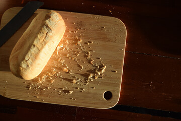 A golden bread roll on a bread board with loose crumbs