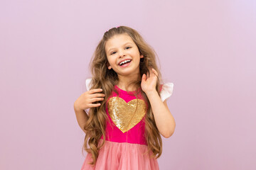 A little girl fluffs her curly, luxurious hair. Isolated pink background.