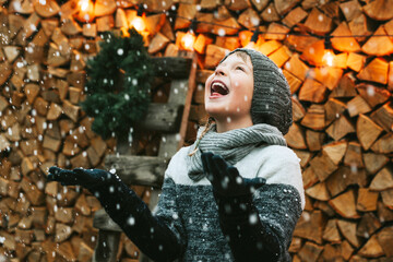 cute boy brother in knitted sweater and hat having fun with first snow and catches snowflakes at...