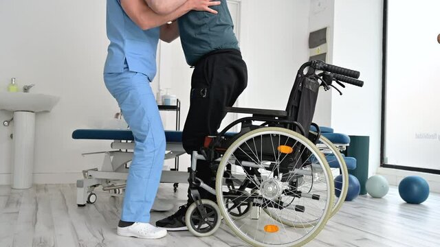 Male Physiotherapist helping a patient with a neurological disease to get up from wheelchair at rehabilitation hospital. High quality 4k footage